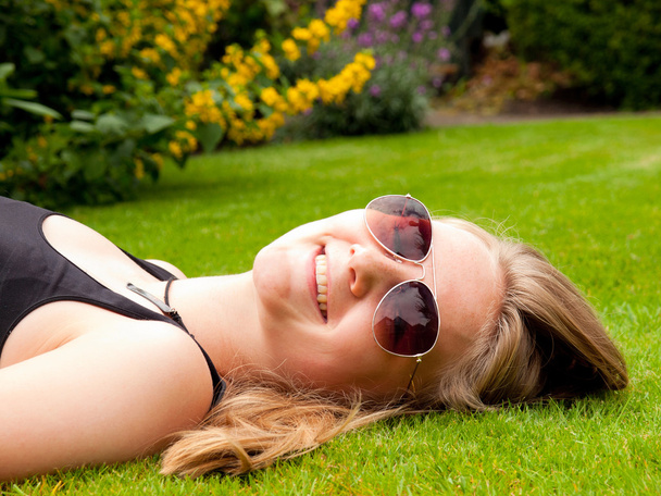 mooie lachende tienermeisje met zonnebril liggend op haar rug - Foto, afbeelding