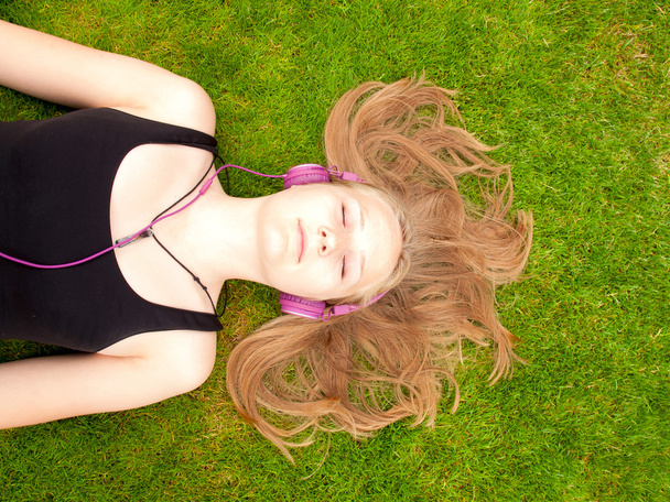 Menina adolescente bonita com fones de ouvido deitado de costas na grama
 - Foto, Imagem