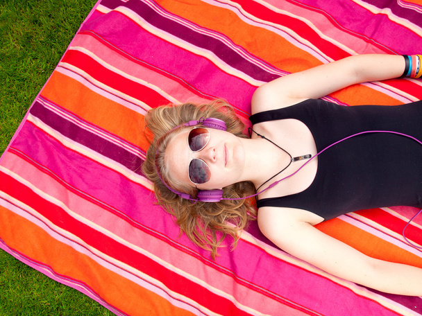 mooie tiener meisje met koptelefoon op haar rug op een kleurrijk tapijt - Foto, afbeelding