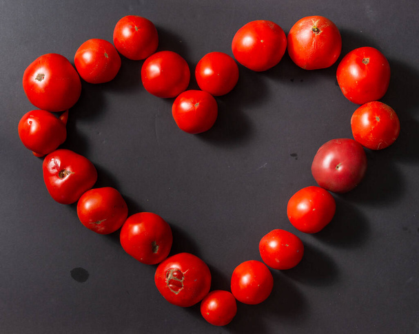 A heart lined with red tomatoes on a black background. - Fotó, kép