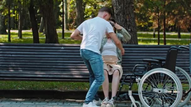 Mann bringt Frau vom Rollstuhl auf Bank - Filmmaterial, Video
