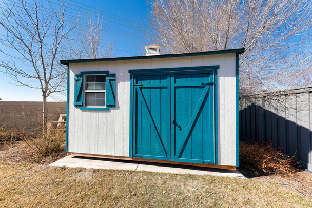 Small tool shed exterior with white wooden wall and blue green double doors and window shutters - Photo, Image