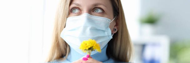 Jovem mulher em máscara médica protetora farejando flor amarela - Foto, Imagem