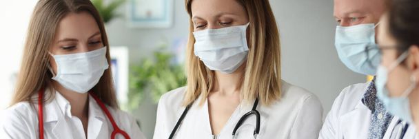 Група лікарів в медичних захисних масках, що стоять з кишенями з документами в клініці
 - Фото, зображення