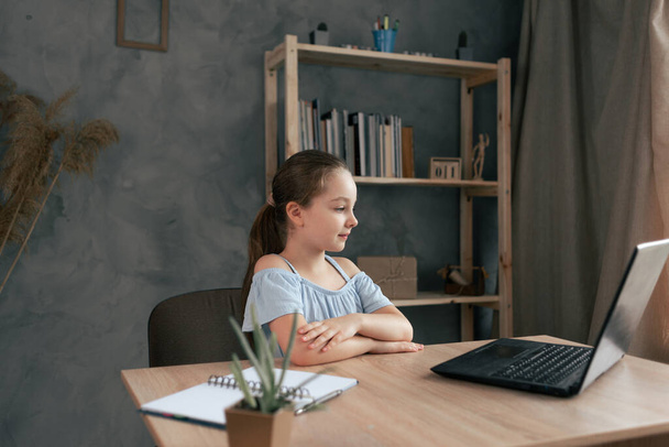 Teenager-Schülerin bei Hausaufgaben mit Laptop zu Hause. Das Kind benutzt Geräte zum Lernen, sitzt am Tisch und schaut sich eine Videostunde oder eine Live-Übertragung an. Kopierraum. - Foto, Bild