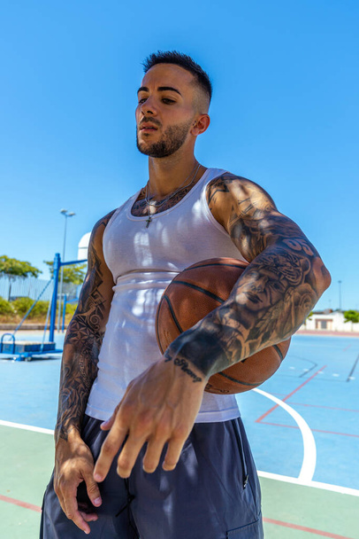 A vertical shot of a sporty Caucasian male with tattoos playing basketball - 写真・画像