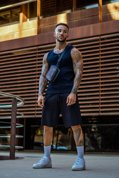 A vertical shot of a Caucasian sporty male with tattoos standing in the street - Photo, Image