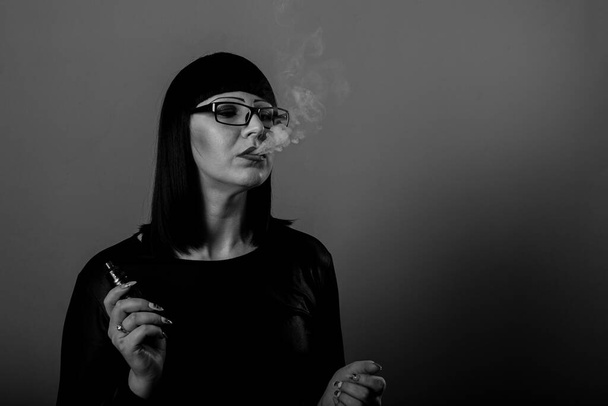 Egy gyönyörű, kifinomult lány élvezi az elektronikus cigaretta füstjét. - Fotó, kép