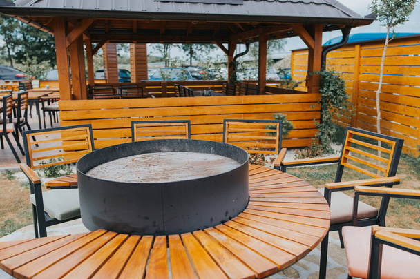 A closeup shot of an outside dining area with a round table and a grill place in the center - Фото, изображение