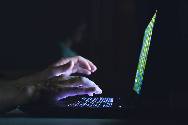 A closeup shot of a male working on his laptop in the darkness - Фото, зображення