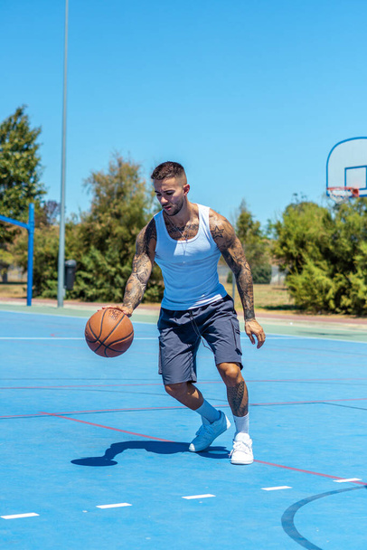A vertical shot of a sporty Caucasian male with tattoos playing basketball - Valokuva, kuva