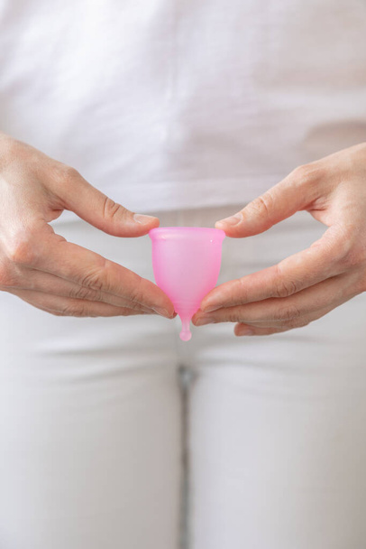 a European woman holds a pink menstrual cup made of silicone in her hands - Фото, изображение