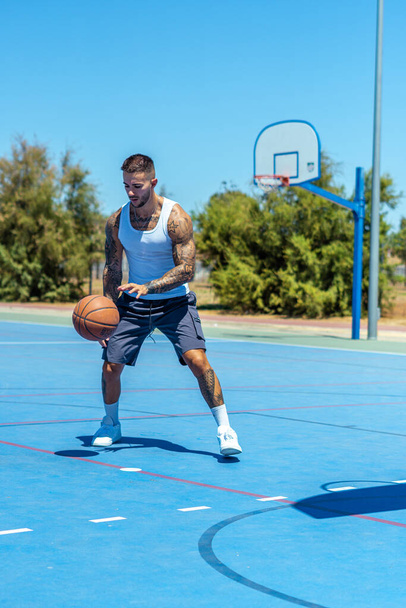 A vertical shot of a sporty Caucasian male with tattoos playing basketball - Fotografie, Obrázek