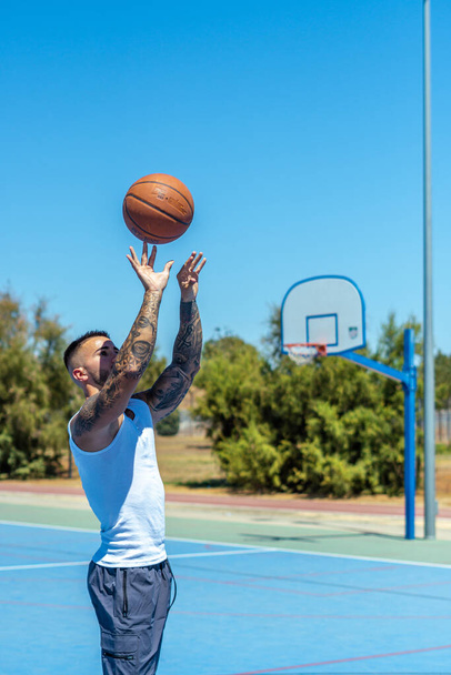 A vertical shot of a sporty Caucasian male with tattoos playing basketball - Фото, изображение
