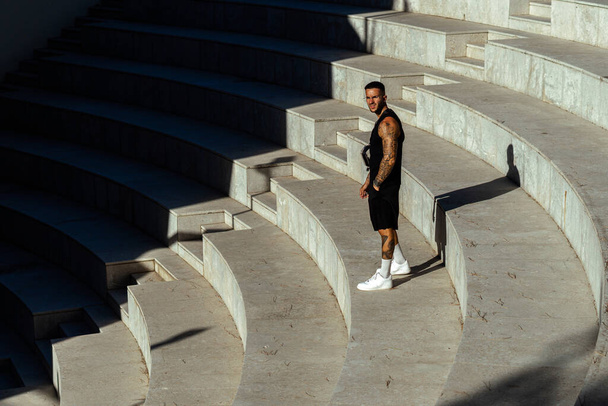 A Caucasian sporty male with tattoos standing in the stone stair architecture - Foto, afbeelding