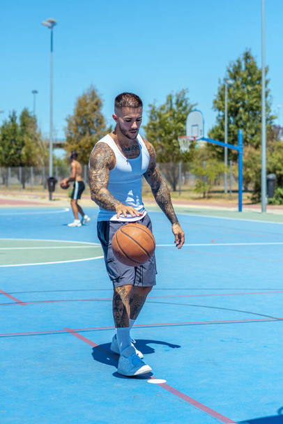 A vertical shot of a sporty Caucasian male with tattoos playing basketball - Foto, imagen