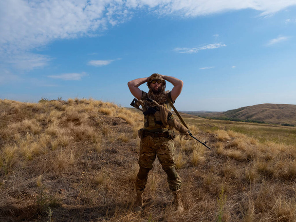 Фото найманця снайпера в камуфляжному одязі під палючим сонцем. Він стоїть з гвинтівкою і досліджує місцевість
. - Фото, зображення