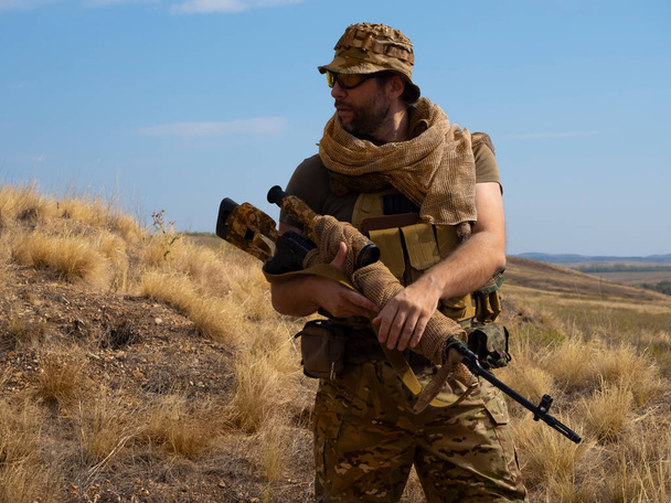 Söldnerheckenschützen in Tarnkleidung unter sengender Sonne. Er steht mit einem Gewehr und erkundet die Gegend. - Foto, Bild