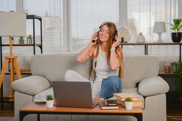 mooie jonge vrouw luisteren naar muziek op de hoofdtelefoon en op zoek naar laptop op de bank thuis - Foto, afbeelding