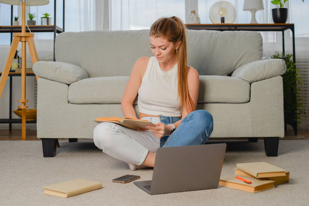 Молодая девушка студентка делает домашнее задание с ноутбуком на дому, онлайн обучение, дистанционное образование - Фото, изображение