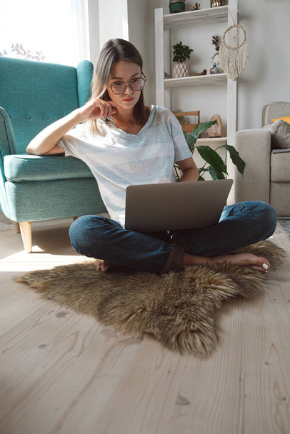 Young woman using laptop to work, sitting on the floor at home. Flexible hours and remote work - Photo, Image