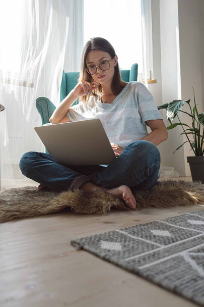 Young woman using laptop to work, sitting on the floor at home. Flexible hours and remote work - Фото, изображение