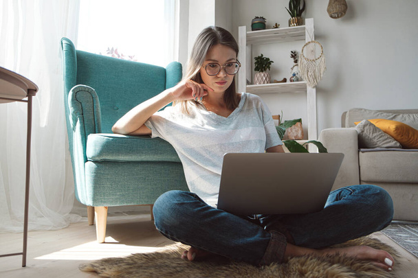 Mujer joven usando el ordenador portátil para trabajar, sentada en el suelo en casa. Horas flexibles y trabajo remoto - Foto, imagen