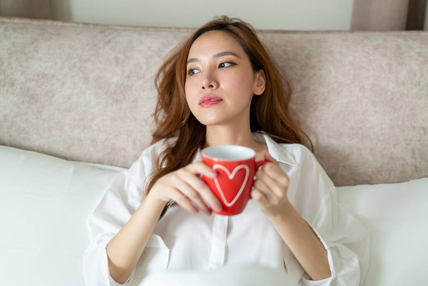 portrait beautiful Asian woman wake up and holding coffee cup or mug on bed in the morning - Fotografie, Obrázek
