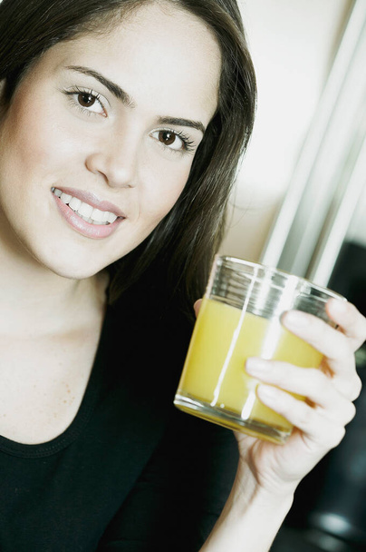 Portrait of a young woman holding a glass of orange juice and smiling - Фото, зображення
