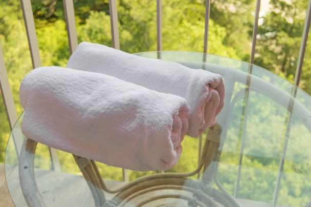 Close-up de dois rolos de toalhas terry branco deitado em uma mesa de vidro transparente na varanda, o efeito de reflexão. - Foto, Imagem