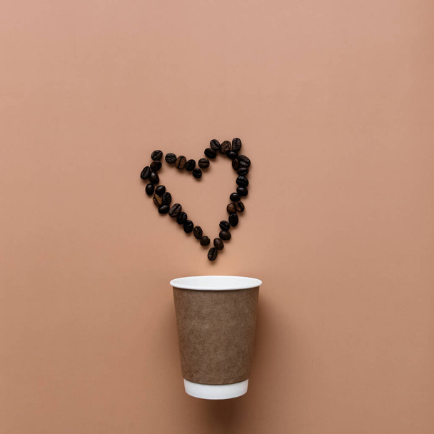 Beige background with paper coffee cup, coffee beans heart shape. High quality photo - Фото, зображення