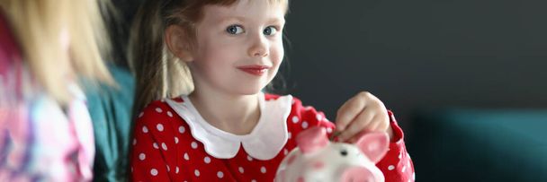 Little girl with her mother throws coin into pink piggy bank - Photo, Image