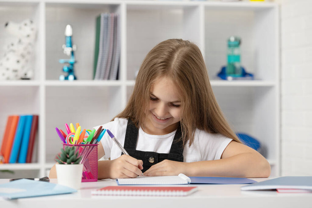счастливый ребенок, пишущий в тетрадке на школьном уроке в школьной форме, возвращается в школу - Фото, изображение