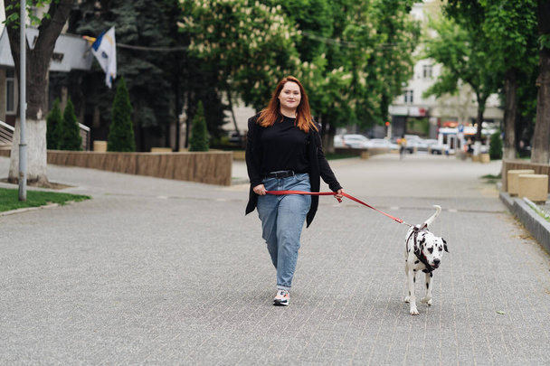 Vrouw wandelen, discussiëren en spelen met haar dalmatiaanse huisdier in de stad - Foto, afbeelding