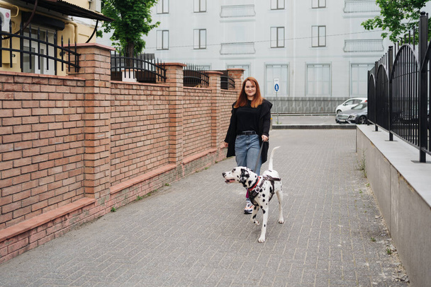 Γυναίκα περπατά, συζητά και παίζει με το Δαλματίας κατοικίδιο ζώο της στην πόλη - Φωτογραφία, εικόνα
