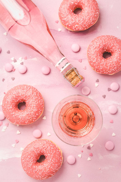 Розовое вино или коктейль с розовыми пончиками и розовыми шоколадными бобами на розовом фоне - Фото, изображение