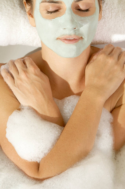Close-up of a young woman wearing a facial mask in a bathtub - Fotó, kép