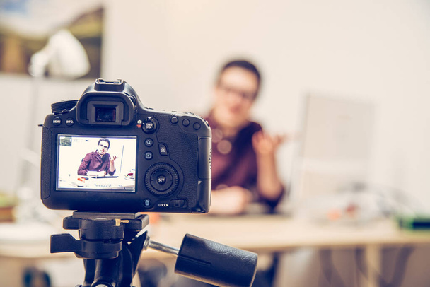 Camera on a tripod filming a blogger at home sitting on his workspace - 写真・画像