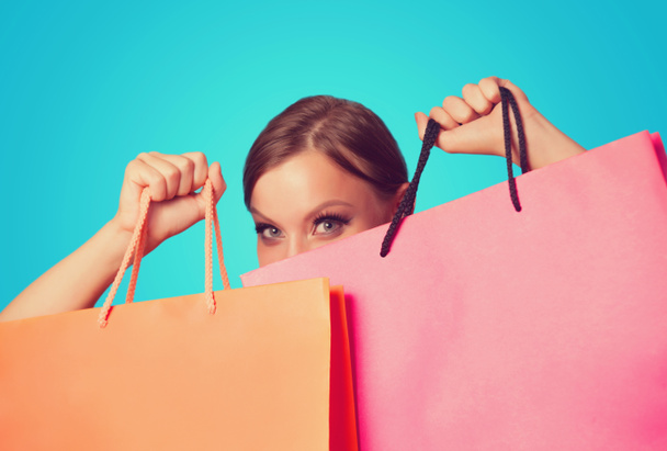 Brunette girl with shopping bags on blue backgorund. - Photo, Image