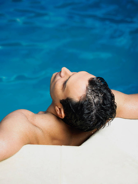 young man in a black bathing suit relaxing in the pool - Foto, imagen