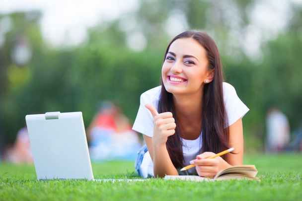 Brunette girl with notebook and book on green grass in the park. - Photo, Image