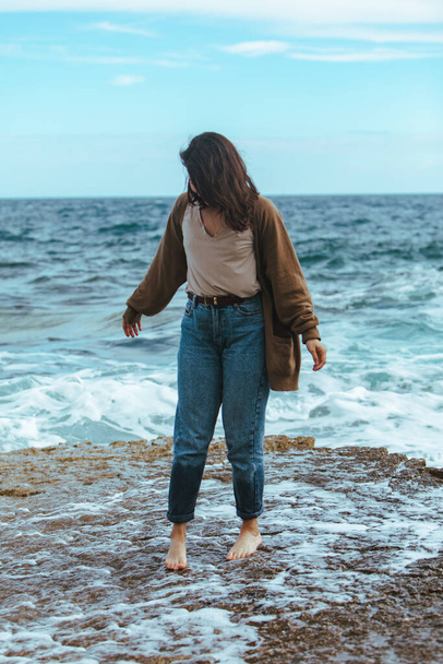 Kobieta chodząca po skalistej plaży w mokrych dżinsach boso. lato morze wakacje - Zdjęcie, obraz