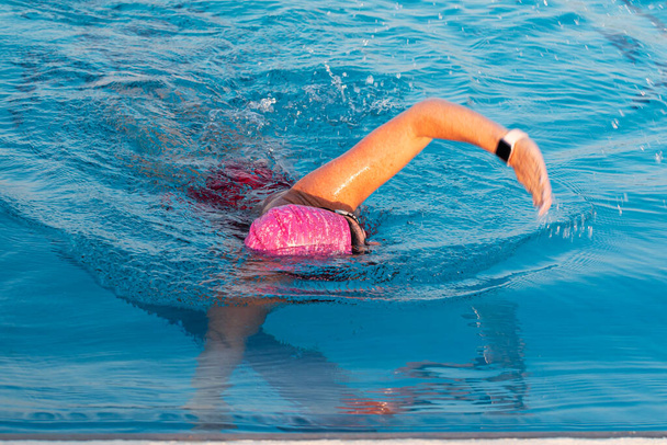 Vista frontal de una nadadora con gorra rosa acercándose a la pared de un entrenamiento de billar para triatlón. - Foto, Imagen