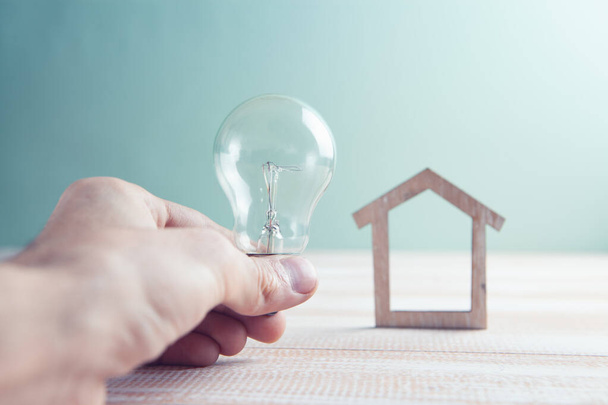 hand holds a light bulb and a small house - Фото, зображення