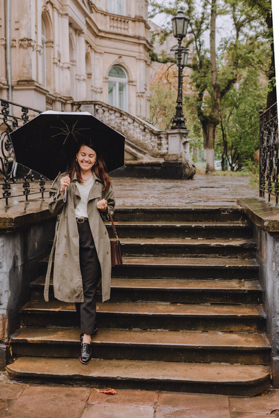 νεαρή όμορφη γυναίκα σε φθινοπωρινή στολή με τα πόδια από δρόμο της πόλης με ομπρέλα σε βροχερές καιρικές συνθήκες. αντίγραφο χώρου - Φωτογραφία, εικόνα