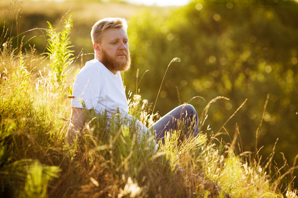 Red-bearded man sitting on the grass - 写真・画像