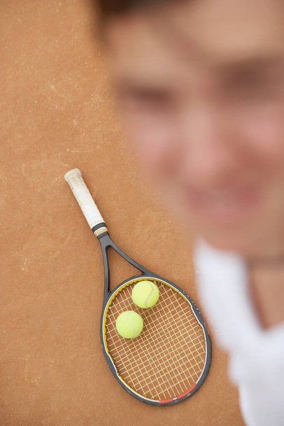Vysoký úhel pohledu na středně dospělého muže se dvěma tenisovými míčky a tenisovou raketou - Fotografie, Obrázek