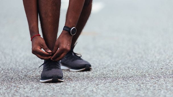 Close up Asian sport runner black man standing he trying shoelace running shoes getting ready for jogging and run at the outdoor street health park, healthy exercise workout concept - Photo, image