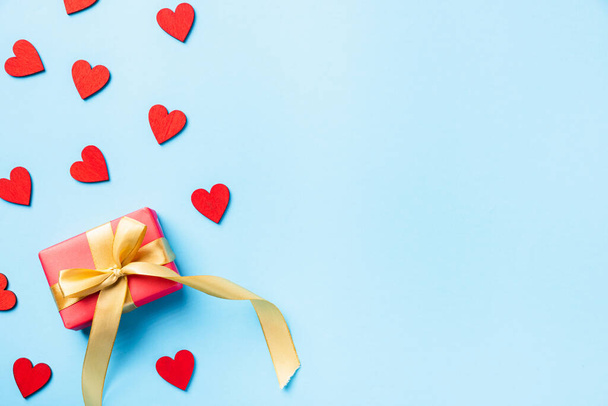 Happy Valentines' day background concept. Red gift box with a golden bow ribbon and wood red hearts composition greeting card for love isolated on blue background with copy space. Top View from above - Φωτογραφία, εικόνα