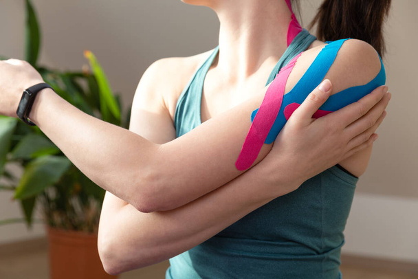 Young fit women wearing kinesio tape on her shoulder. Performing exercise at home. Kinesiology physical therapy. - Foto, Imagem